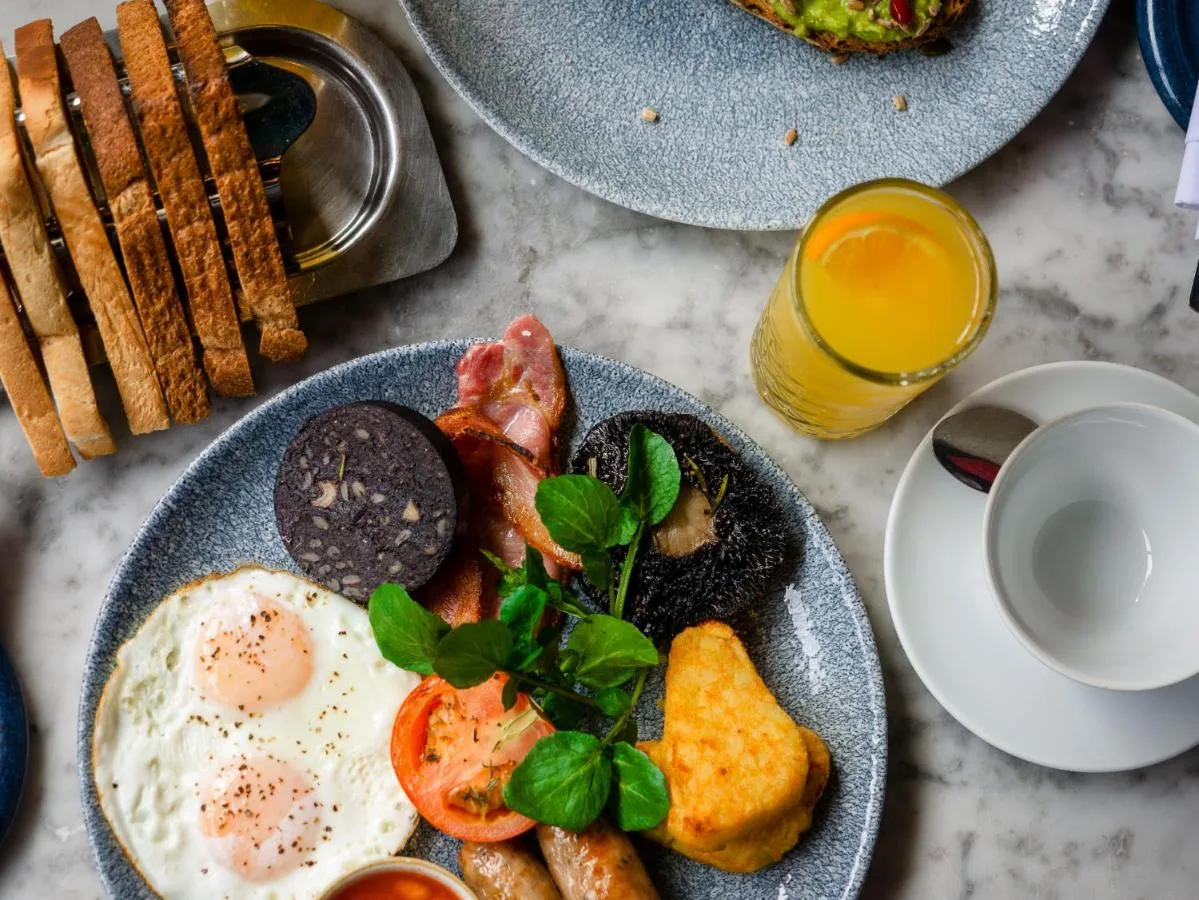 a table with two plates of breakfast food and a glass of orange juice at Apex Grassmarket Hotel in Edinburgh